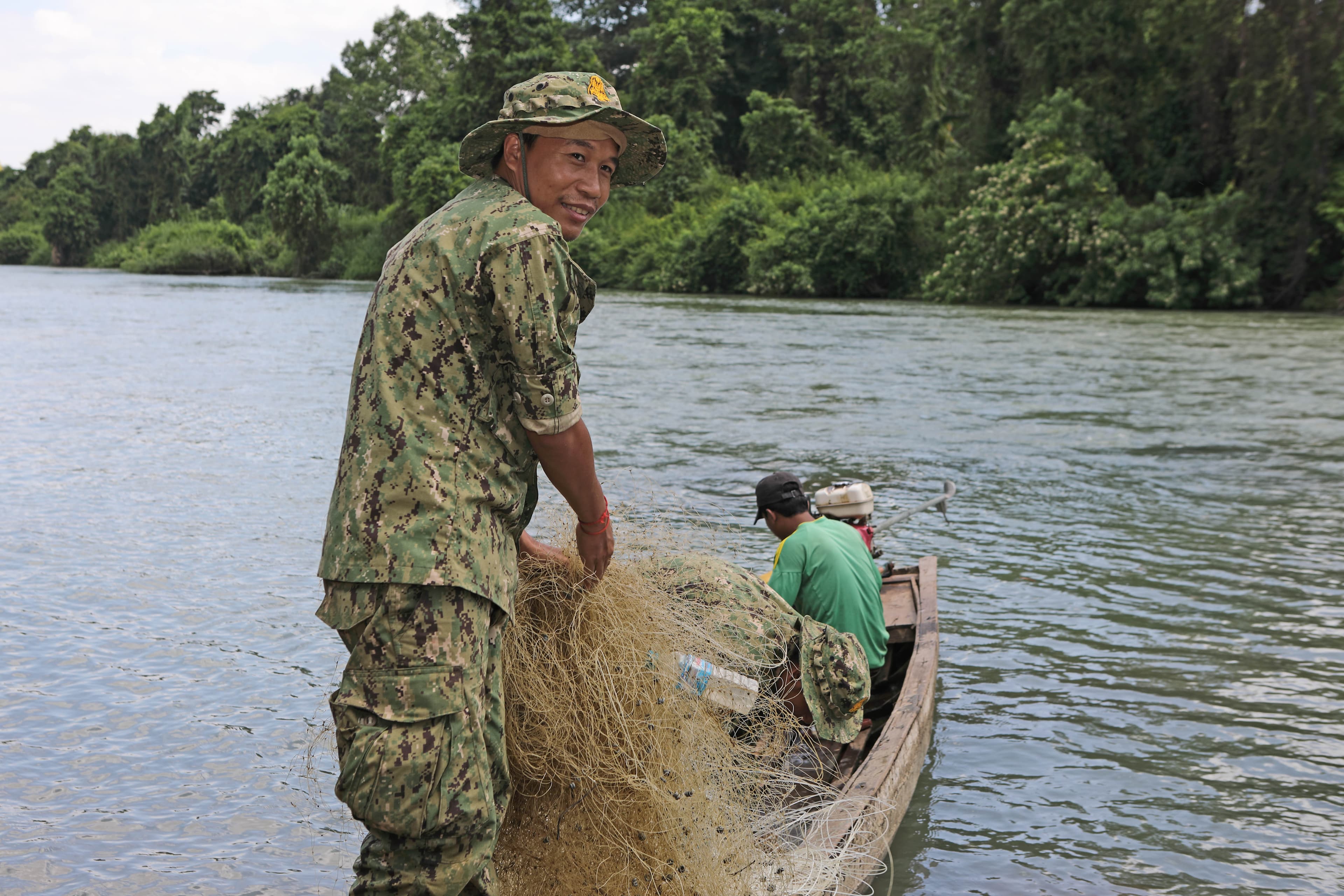A ranger working from a boat beside a forested river.